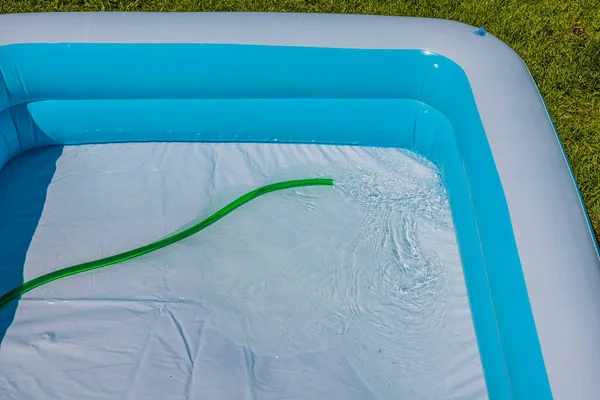 Close up view of children\'s swimming pool being filled with water from garden hose.