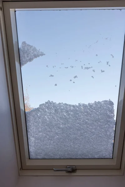 View of interior of snow-covered dormer window on roof of house from room covered with snow on frosty winter day. Sweden.