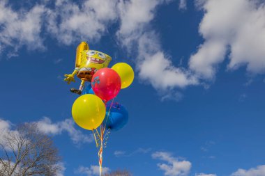 Beyaz bulutlu mavi gökyüzüne karşı rüzgarda gelişen çocuklar için festival balonları. İsveç Uppsala. 01.01.2023.