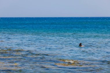 Beautiful view of rocky coast of Mediterranean Sea and man in snorkeling mask on blue sea water surface. Greece. 