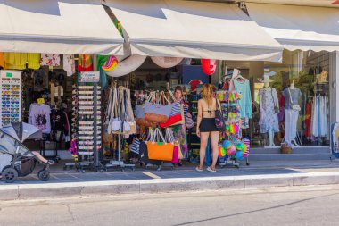 View of young woman looking at tourist goods placed outside of souvenir boutique. Greece. Rhodes. 08.25.2022.