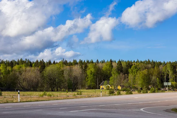 View of landscape of nature with villas on edge of forest along highway against blue sky with white clouds. Sweden.
