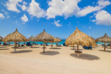 Beautiful view of Atlantic Ocean and people on Eagle Beach with sun loungers and umbrellas against blue sky with white clouds. Aruba.
