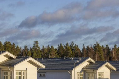 Beautiful view of new white wooden houses on green forest trees and blue sky with light gray clouds.  Sweden. Uppsala. Europe. 