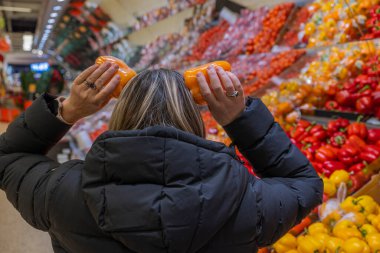Sebze süpermarketinde portakallı biberle oynayan bir kadının komik manzarası. İsveç.