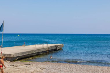 Sıcak yaz gününde Akdeniz kıyısında suda oturan küçük bir kız görüntüsü. Yunanistan. Rodos. 08.25.2022.