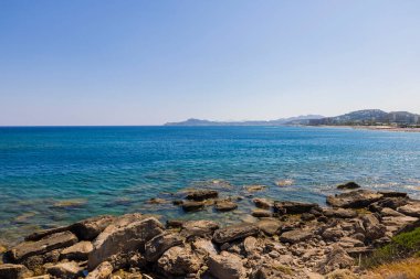Akdeniz 'in taş sahili ve ufukta oteller var. Yunanistan.