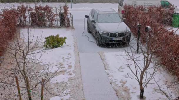 早春の降雪中にBmw Ix3電気自動車を充電して民家の駐車場の眺め スウェーデンだ ウプサラ 2023 — ストック動画