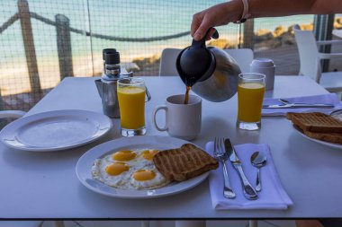Kahvaltı sırasında Atlantik Okyanusu manzaralı açık hava restoranında fincana kahve dökerken yakın çekim görüntüsü. Aruba.