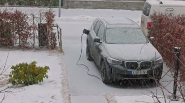 Baharın başında evin özel otoparkında BMW iX3 elektrikli araba şarj olurken yakın çekim görüntüsü. İsveç. Uppsala. 03.21.2023.