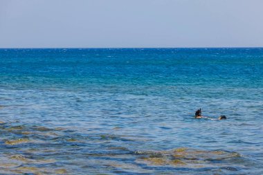 Akdeniz 'in kayalık kıyı manzarası ve mavi deniz su yüzeyinde şnorkelle yüzen adam. Yunanistan. 