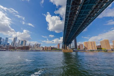 Hudson Nehri üzerindeki Brooklyn Köprüsü ve Manhattan 'ın gökdelenlerine karşı beyaz bulutlu mavi gökyüzü. ABD. New York.