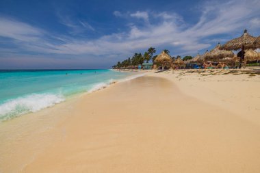 Atlantik Okyanusu 'nun güzel manzarasında kumlu kartal sahilinde güneş şemsiyeleri altında uzanan insanlar. Aruba. Oranjestad. 03.21.2023.