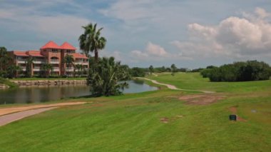 Otel binasının muhteşem manzarası ve gölün mavi su yüzeyi. Arka planda yeşil golf sahaları var. Mavi gökyüzü ve beyaz bulutlar. Aruba.