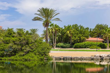 Beautiful view of hotel building in park with palm trees and lake. Aruba.