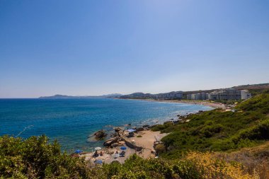 Güneşli yaz gününde arka plandaki otellerde kayalık sahil sahilindeki insanların güzel manzarası. Yunanistan. Rodos.