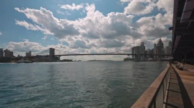 Brooklyn Köprüsü 'ne bakan Manhattan rıhtımının güzel manzarası, beyaz bulutlu mavi gökyüzüne karşı geçen tekneler..