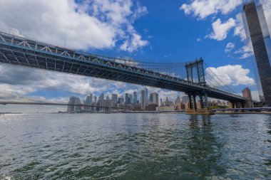 Hudson Nehri üzerindeki Brooklyn Köprüsü ve Manhattan 'ın gökdelenlerine karşı beyaz bulutlu mavi gökyüzü. - New York. ABD.