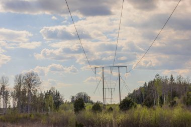 Yüksek voltajlı elektrik iletim hattının mavi gökyüzüne karşı beyaz bulutlu arka plan görüntüsü. İsveç.