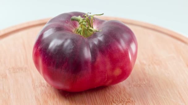 木製の切断ボード上のトマトの成熟した黒の品種の回転のマクロビュー孤立した背景 — ストック動画