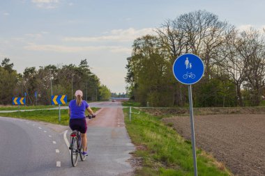Bisikletli bir kadının bisiklet yolunda hareket edişinin güzel manzarası. İsveç.