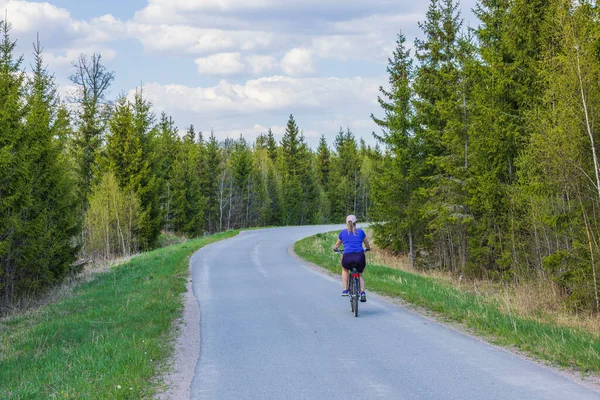 Beautiful view of woman on bicycle on countryside road on bright summer day. Sweden.