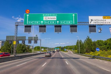Yeşil ağaçlar ve mavi gökyüzü ile birleşen otoyol üzerindeki büyük yol işaretlerinin görüntüsü. İsveç. Avrupa. 
