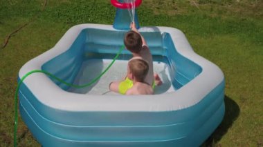 Young boys in inflatable outdoor swimming pool bathe with water on warm summer day. Sweden.