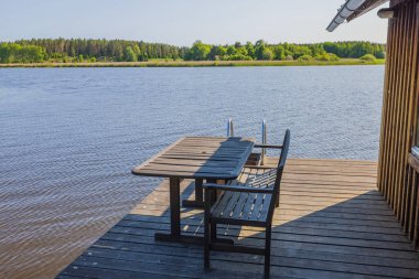 Göl kıyısındaki verandanın ahşap masa ve bank ile yakın görüntüsü. İsveç.