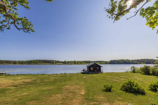 stock image Beautiful view of small utility house on lake shore on blue sky background. Sweden, Europe. 