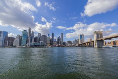 Hudson Nehri 'nden Brooklyn Köprüsü' ne uzanan Manhattan 'ın güzel manzarası. Arkaplanda beyaz bulutlu mavi gökyüzü. - New York. ABD.