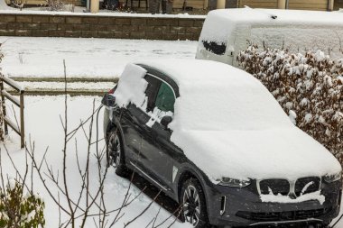 Kış günü özel otopark villasında karla kaplı elektrikli araba görüntüsü. İsveç.