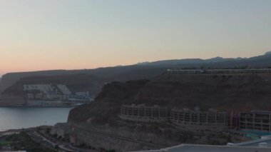 Atlantik Okyanusu 'ndaki dağ kıyısındaki binaların günbatımının arkaplanındaki güzel manzarası. Büyük Kanarya. İspanya.