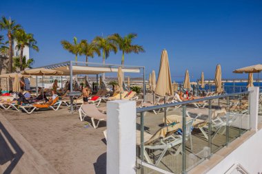 İnsanlar havuz kenarındaki güneşli yataklarda otelin masasında oturuyorlar. Büyük Kanarya, İspanya.