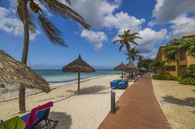 Atlantik Okyanusu 'nun muhteşem kıyı manzarası. Kıyı şeridi boyunca beyaz bulutlu mavi gökyüzü boyunca uzanan güneşli yataklı bir otel. Aruba. 