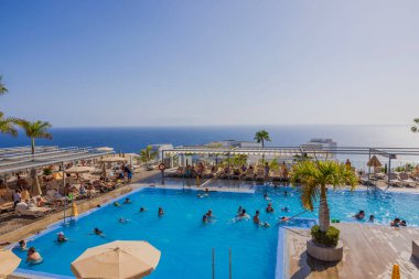 Atlantik Okyanusu 'nda günbatımının arka planında insanların olduğu güzel bir otel havuzu manzarası. Büyük Kanarya, İspanya. 