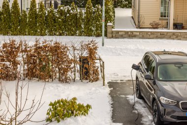 Kış günü elektrik santralinden elektrikli arabaya bağlı özel villadaki otopark manzarası. İsveç.