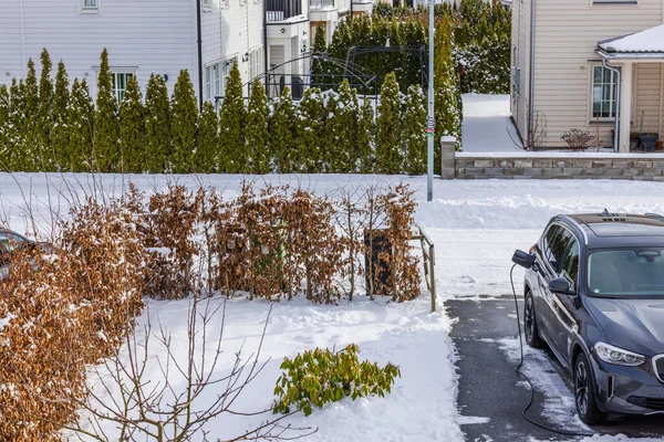 Güneşli kış gününde elektrik kablosuyla bağlı elektrikli araçla özel evdeki otopark manzarası. İsveç.