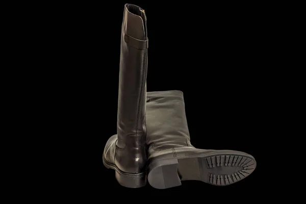 Close-up view of black leather knee-high boots isolated on black background.