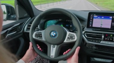 BMW iX3 M-spor elektrikli otomobilin içi çok güzel bir manzara. Otoyol boyunca saatte 100 km hızla ilerliyor. Araçta kadın sürücü. 