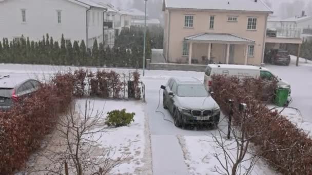 春の冬の降雪中に充電ステーションからケーブルで接続された電気自動車Bmw Ix3の家での駐車場の眺め — ストック動画