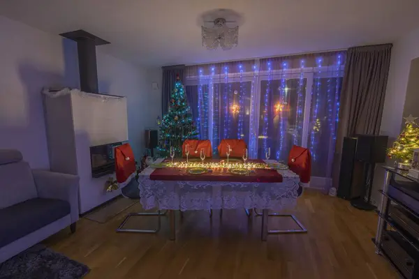 Beautiful night view of interior of room with glowing garland on window, Christmas tree and served table. Sweden.