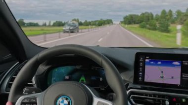 BMW iX3 M-spor elektrikli aracın kadın sürücüyle otoyol boyunca sürüşünü görüntüle. 
