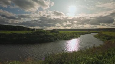 Günbatımında tarımsal tarlalar arasında akan dar nehirli sonbahar manzarası. İsveç.