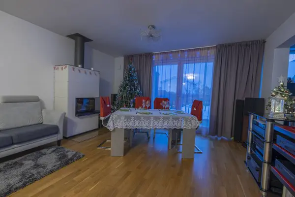 Beautiful view of interior of room with served Christmas table, natural Christmas tree and view through panoramic window of garden covered with snow. Sweden.