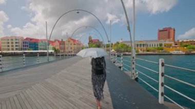 Kadın, kendisini ultraviyole radyasyondan koruyan şemsiyeli kavurucu güneşten korumak için kaygan köprü boyunca yürür.. 