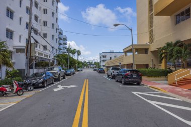Miami Beach caddelerinden birinin, her iki tarafında park etmiş arabaların, mavi gökyüzünün arka beyaz bulutlu manzarası. Florida, ABD. 