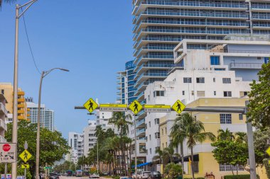 Vurgulanmış uzun yaya geçidi tabelası, yüksek binaları ve mavi gökyüzü olan Miami Beach sokaklarından birinin üzerinde asılı duruyor. Miami Plajı. ABD. 