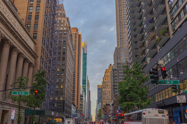 View of 36th Street in Manhattan with skyscrapers and bustling with transportation, set against backdrop of blue sky with white clouds. New York. USA.