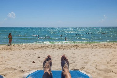 Erkek ayağının güneş yatağında ön plana odaklanmış ve Atlantik okyanus suyunun bulanık arka planına yakın plan. Miami Beach, ABD.